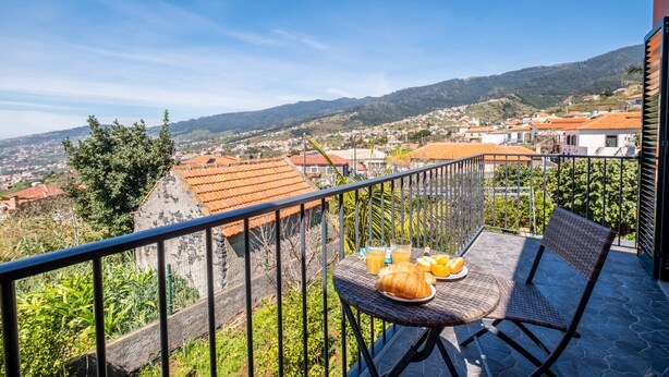 En balkon med et morgenmadsbord, der giver udsigt over en by med røde tage og et kig til bakkerne.