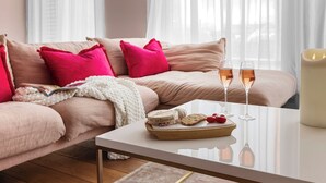 Ett mysigt vardagsrum med en beige soffa, ljusrosa kuddar, ett vitt soffbord och ett ljus.