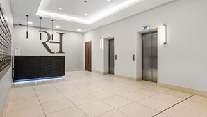 En rymlig entréhall med en receptionsdisk, två hissar och ett klinkergolv.