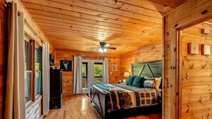 A wooden cabin bedroom with a bed, a ceiling fan, and a view of the outdoors. - New Listing! Mountain Views! 3B/3Ba Sleep 6-7, Hot Tub, Close to Everything! (Sevierville)