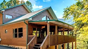 A wooden cabin with a porch, a staircase, and a view of the surrounding forest. - New Listing! Mountain Views! 3B/3Ba Sleep 6-7, Hot Tub, Close to Everything! (Sevierville)