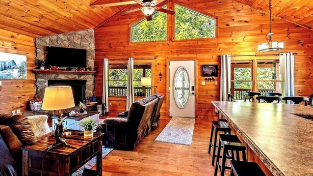 A log cabin interior with a stone fireplace, wooden ceiling, and a dining area. - New Listing! Mountain Views! 3B/3Ba Sleep 6-7, Hot Tub, Close to Everything! (Sevierville)