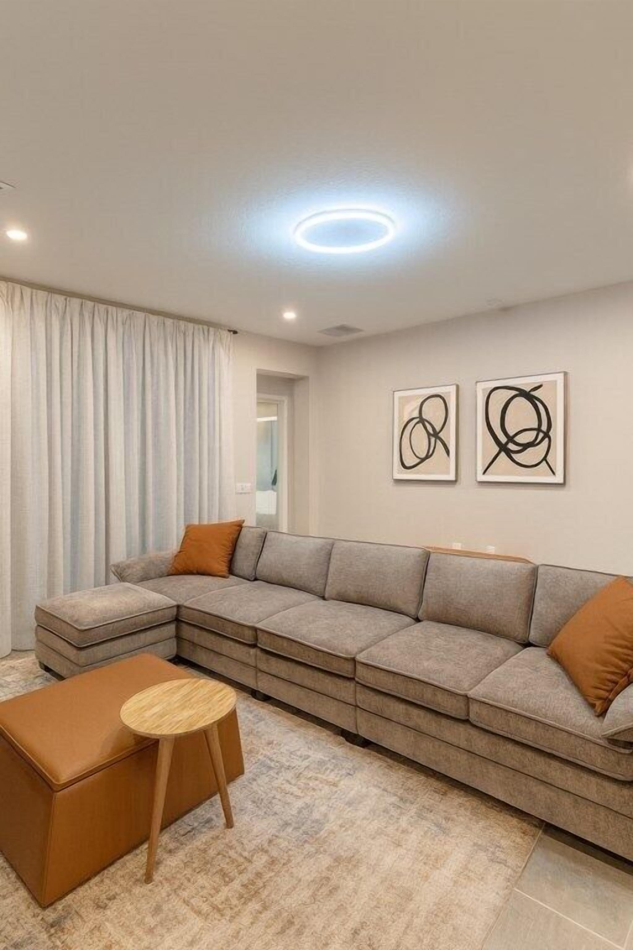 A modern living room with a sectional sofa, a small round table, and two abstract wall art pieces.
