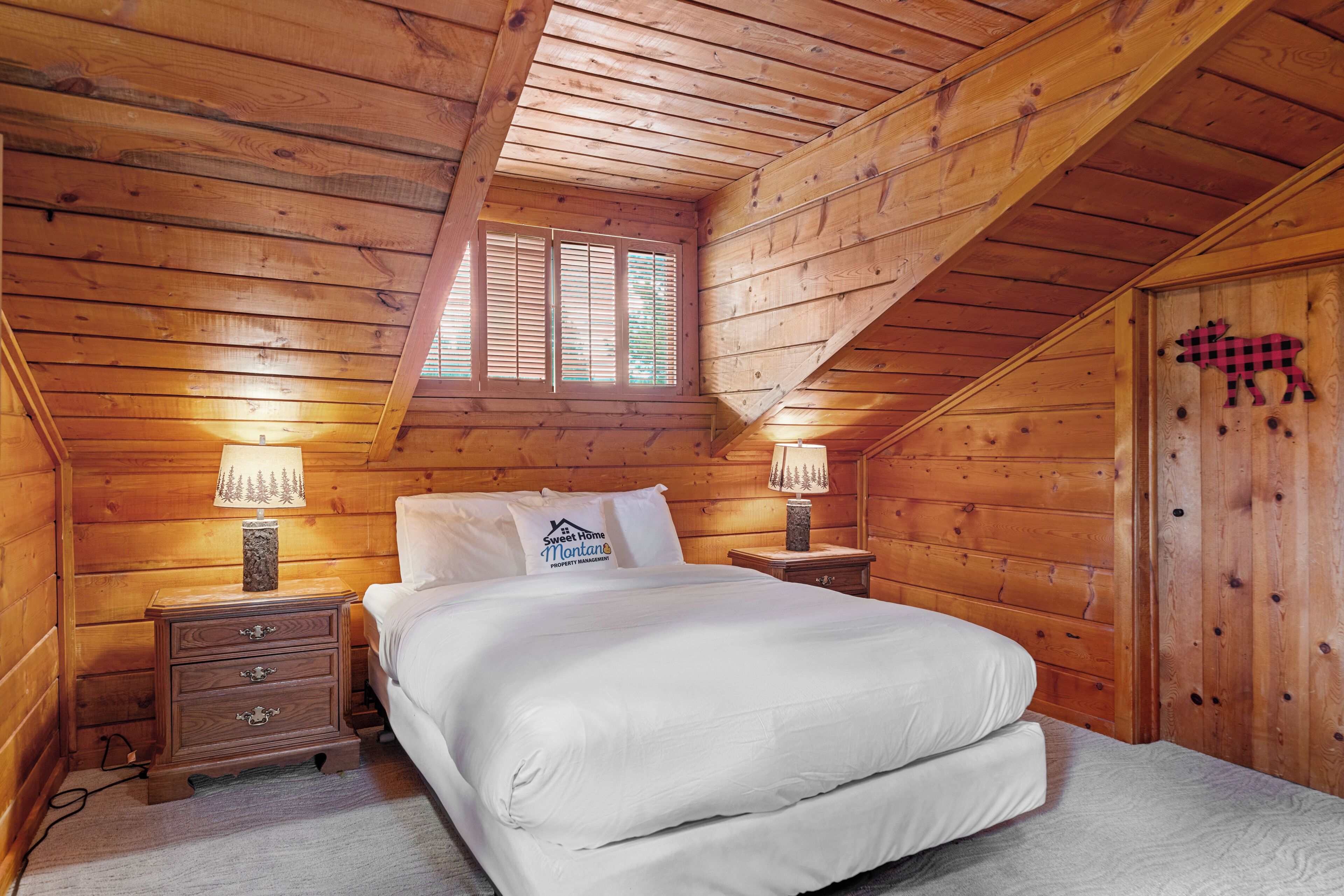 Camera da letto con rivestimento in legno, un letto, due comodini, una finestra e una porta a quadri.