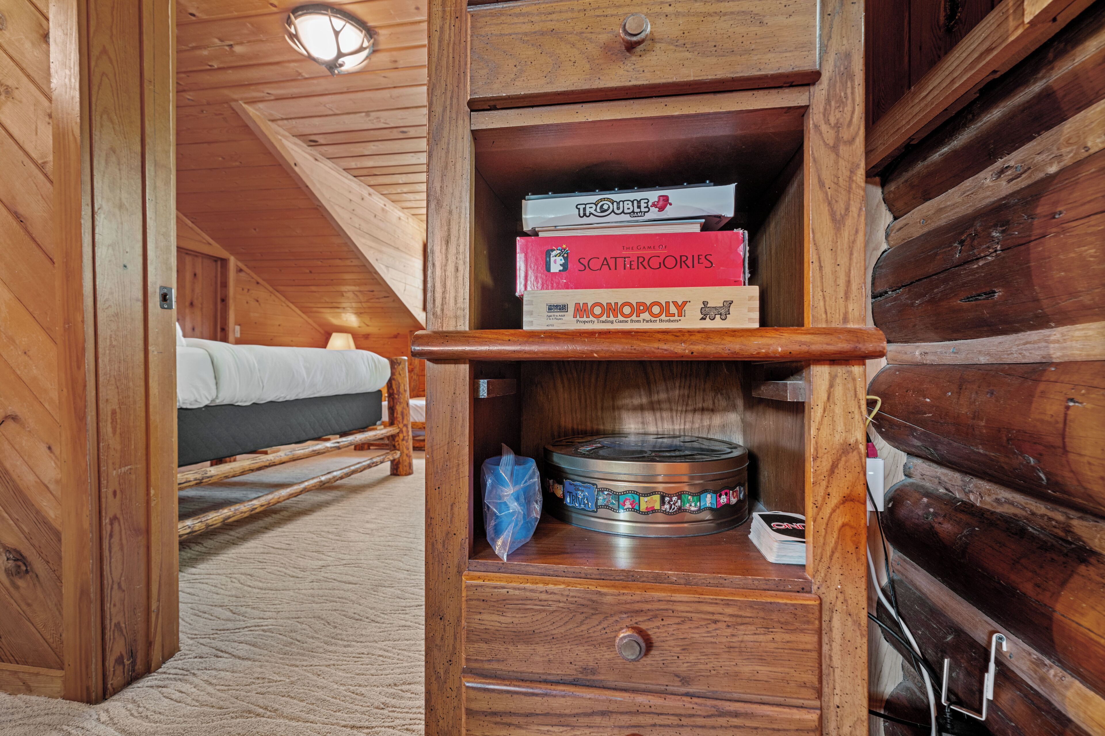 A wooden interior with a bed, a shelf with board games, and a circular table.