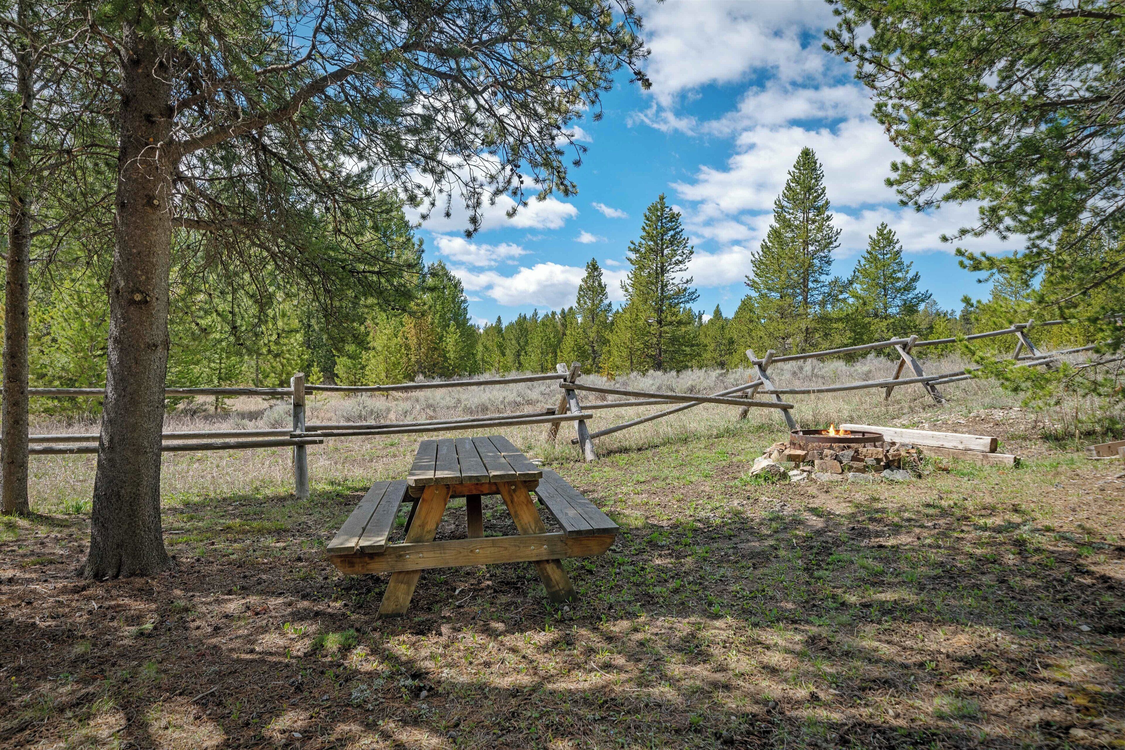A picnic table in a forested area with a wooden fence and trees in the background.