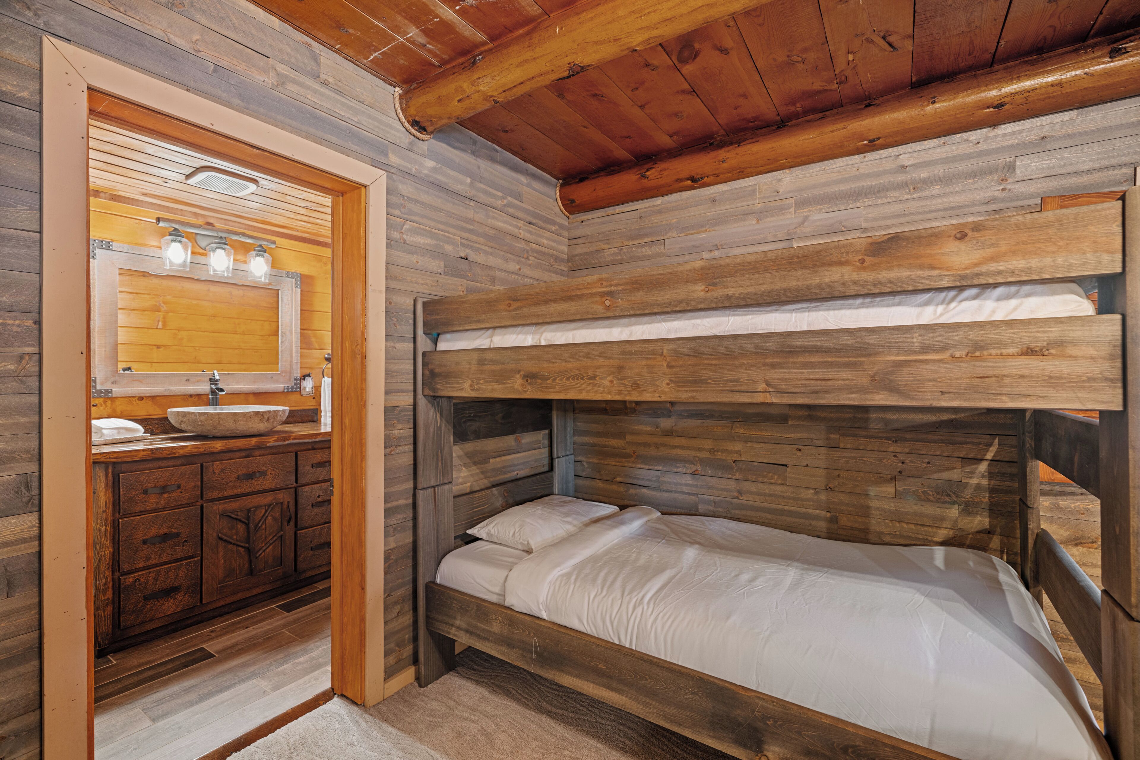 Un letto a castello con testiera in legno, una toeletta in legno con lavandino e uno specchio illuminato.