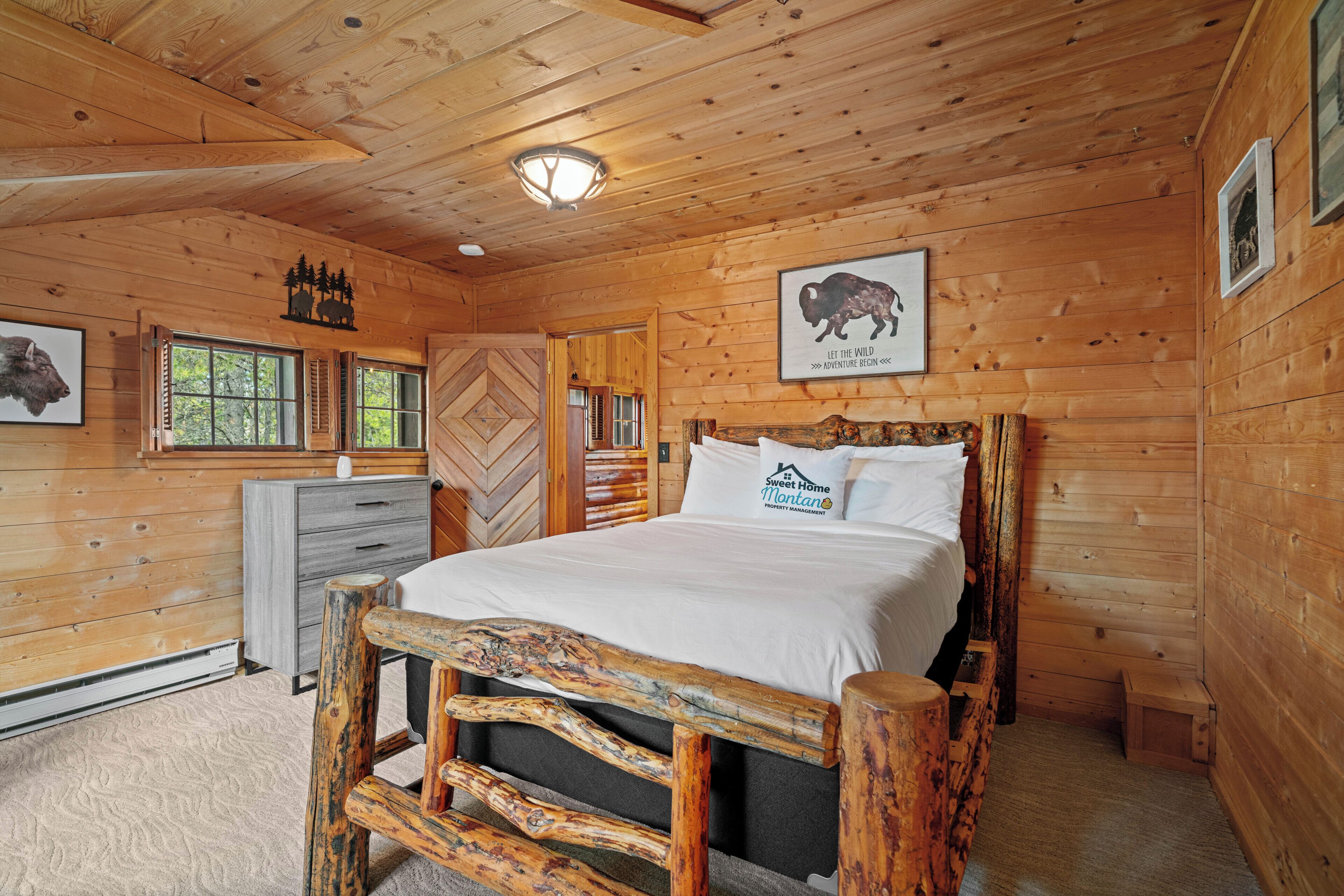 A wooden cabin bedroom with a bed, a dresser, and a window.