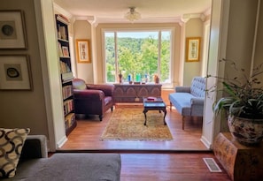 A living room with a sofa, armchair, coffee table, and bookshelf. - Historic Carrie Tucker Cottage with view of Spring River in charming Hardy, Ark. (Hardy)