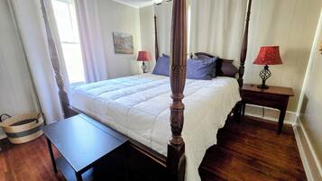 Een hemelbed met houten hoofdeinde, een nachtkastje met lamp en een schilderij aan de muur.