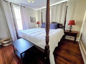 A four-poster bed with a wooden headboard, a bedside table with a lamp, and a painting on the wall.