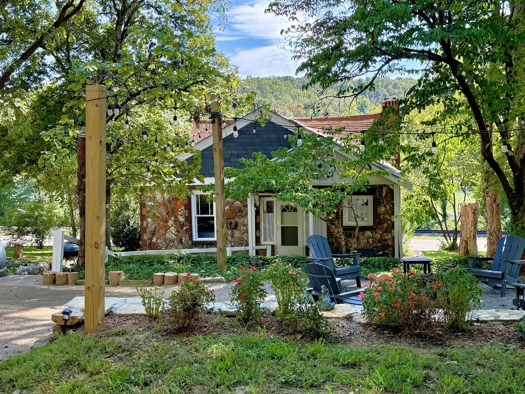 Un chalet rustique aux murs de pierre, entouré d’une végétation luxuriante et doté d’un espace extérieur aménagé pour s’asseoir.