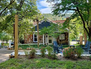 A rustic cabin with a stone exterior, surrounded by lush greenery and outdoor seating.