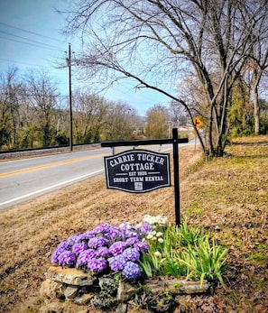 A sign for Carrie Tucker Cottage, a short-term rental property established in 1928, with a road and a warning sign nearby. - Historic Carrie Tucker Cottage with view of Spring River in charming Hardy, Ark. (Hardy)