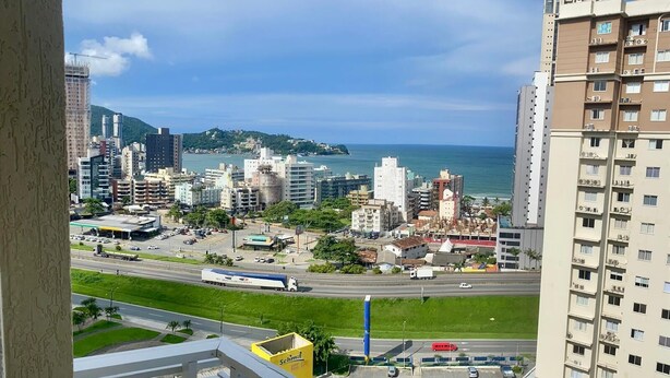 Un immeuble de grande hauteur, doté de nombreux étages, d’un parking et offrant une vue sur un paysage urbain côtier, avec des bâtiments et une plage.