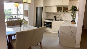 Une cuisine moderne dotée d’un plan de travail en marbre, d’un four encastré et d’un réfrigérateur. On y trouve une table à manger avec des chaises, et un luminaire suspendu au-dessus.