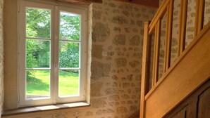Una habitación con pared de piedra, escalera de madera y ventana con vistas a la vegetación.