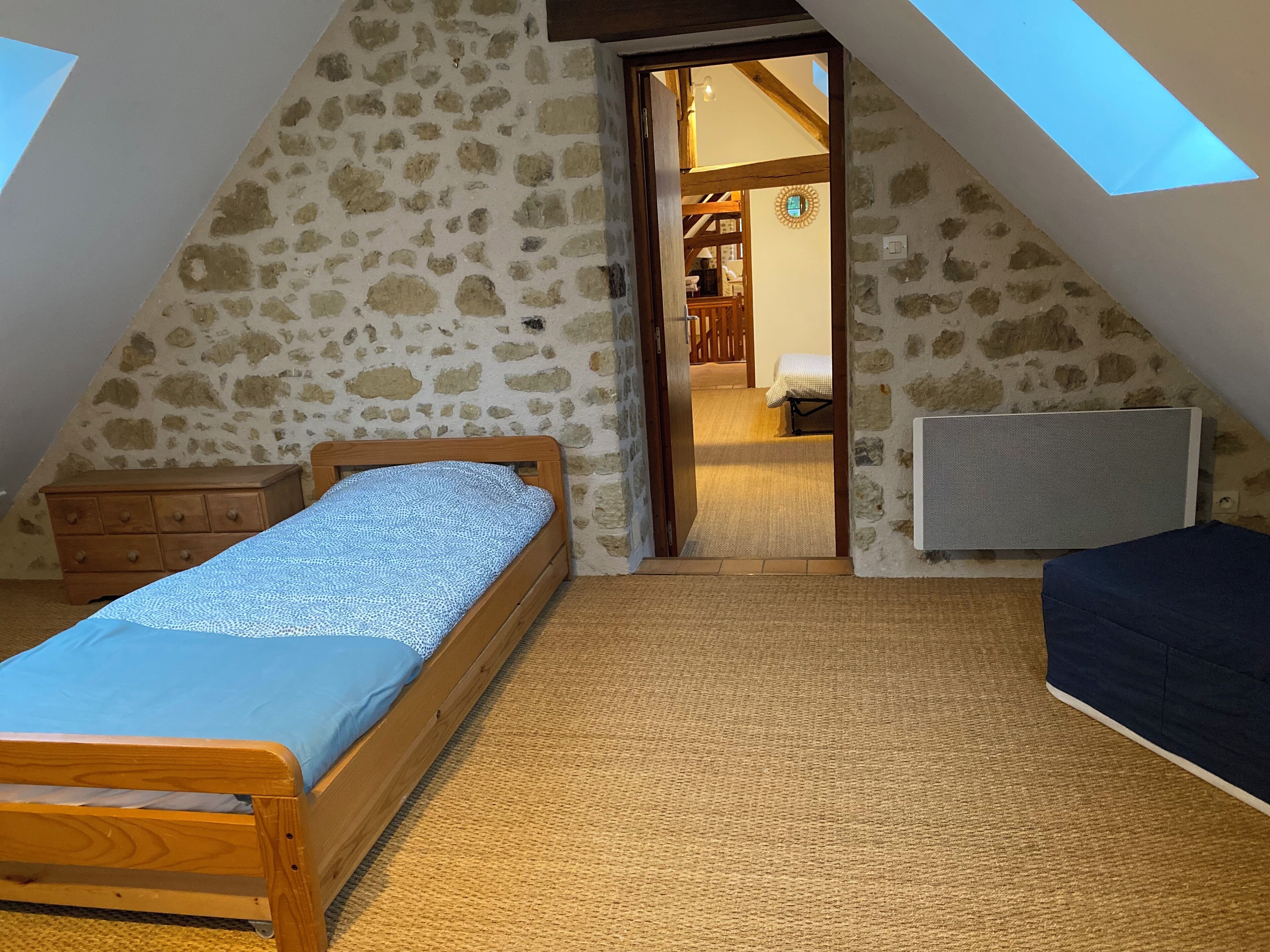 Une petite chambre mansardée avec un toit en pente, comprenant un lit en bois, une petite commode et un canapé bleu.
