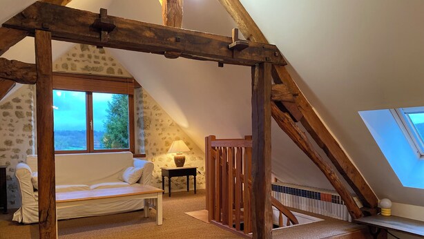 Un dormitorio acogedor en el ático con techo inclinado, un banco de madera, una cama y un ventanal con vistas a un área boscosa.