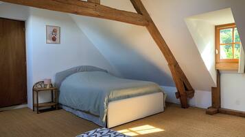 Une chambre avec un plafond en pente, un lit, une table de chevet avec une lampe et une fenêtre donnant sur un paysage verdoyant.