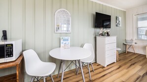 A room with a white table, two white chairs, a white cabinet, a flat-screen TV mounted on the wall, and a wooden floor. - 2 Blocks to Beach | Downtown OC +  1 Parking Space (Ocean City)