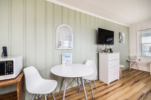 Ein Zimmer mit einem weißen Tisch, zwei weißen Stühlen, einem weißen Schrank, einem an der Wand befestigten Flachbildfernseher und einem Holzboden.