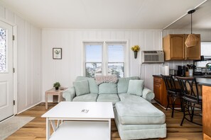 Ein modernes Wohnzimmer mit einem Ecksofa, einem kleinen Tisch und einer Küchenzeile mit Holzschränken sowie einem Esstisch.