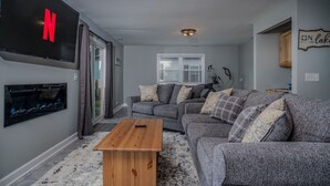 Ein Wohnzimmer mit grauem Sofa, einem Holztisch, einem Kamin und einem flachbildfernseher an der Wand.