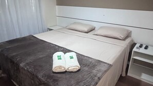 Una habitación de hotel con una cama grande, una mesita de noche con lámpara y una ventana con cortinas.