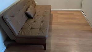 Una habitación con sofá de cuero marrón, panel blanco montado en la pared y suelo de madera.