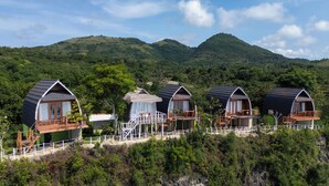 A row of cabins with balconies, surrounded by lush greenery and mountains.