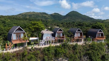 A row of cabins with balconies, surrounded by lush greenery and mountains.