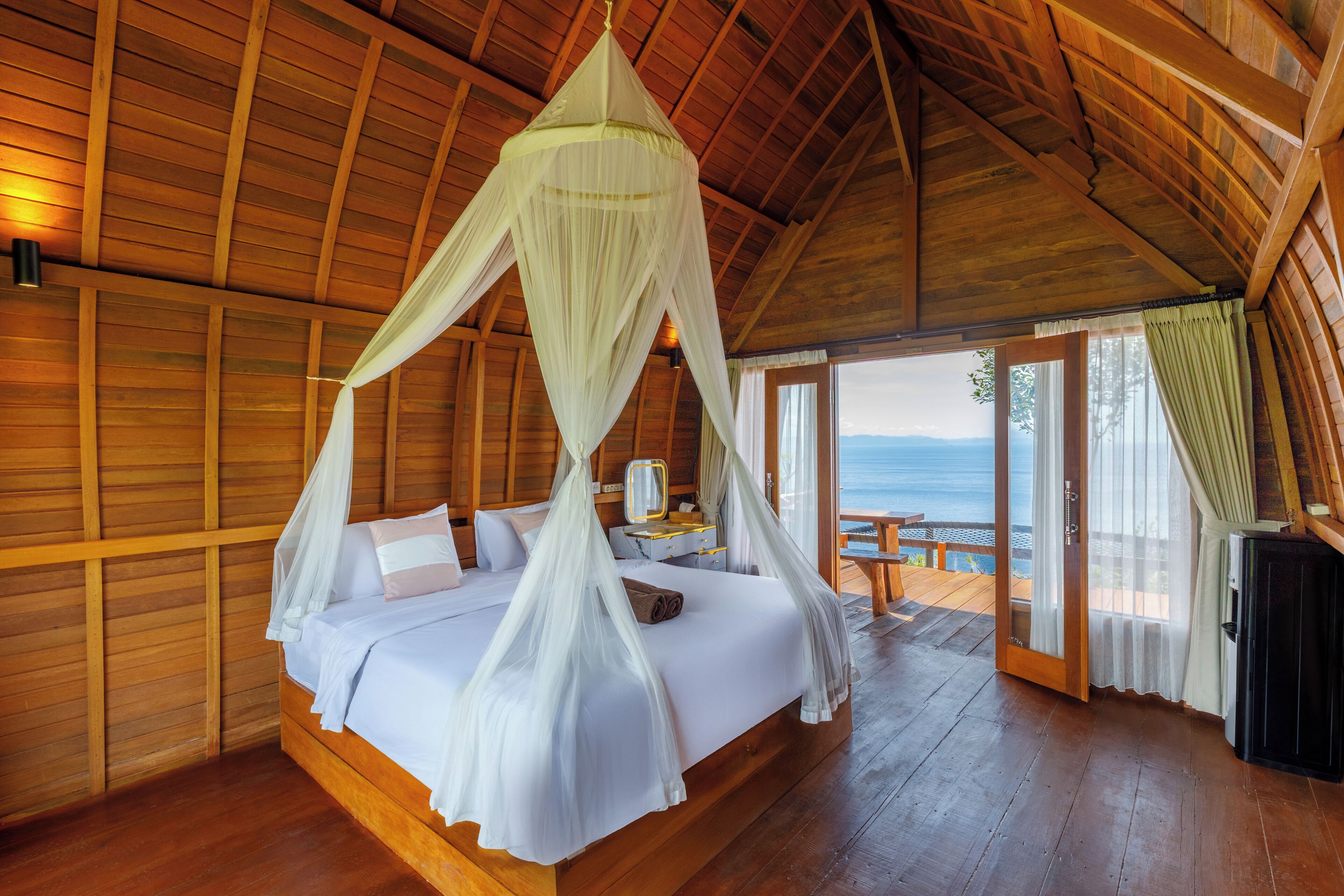 A wooden room with a bed, a nightstand, and a view of the ocean.