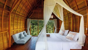 Una habitación con cama, una banca y un gran ventanal con vistas a follaje.