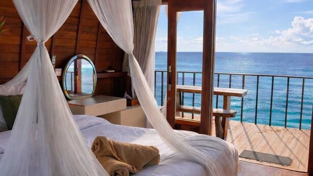 Una habitación con una cama, un osito de peluche, un espejo y vistas al océano.