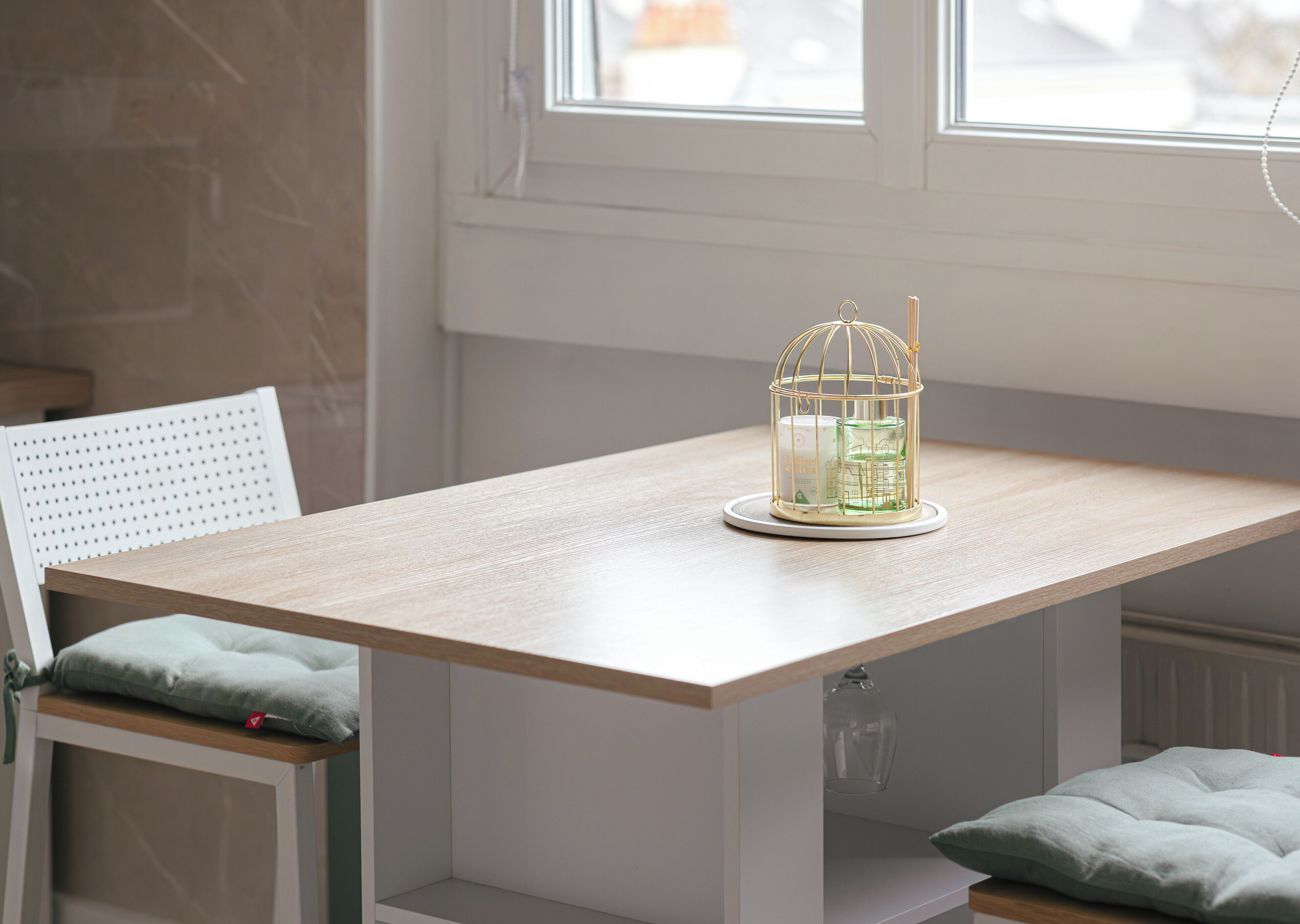 A wooden table with a white chair and a green cushion. A glass candle holder with a candle and a matchbox is on the table.