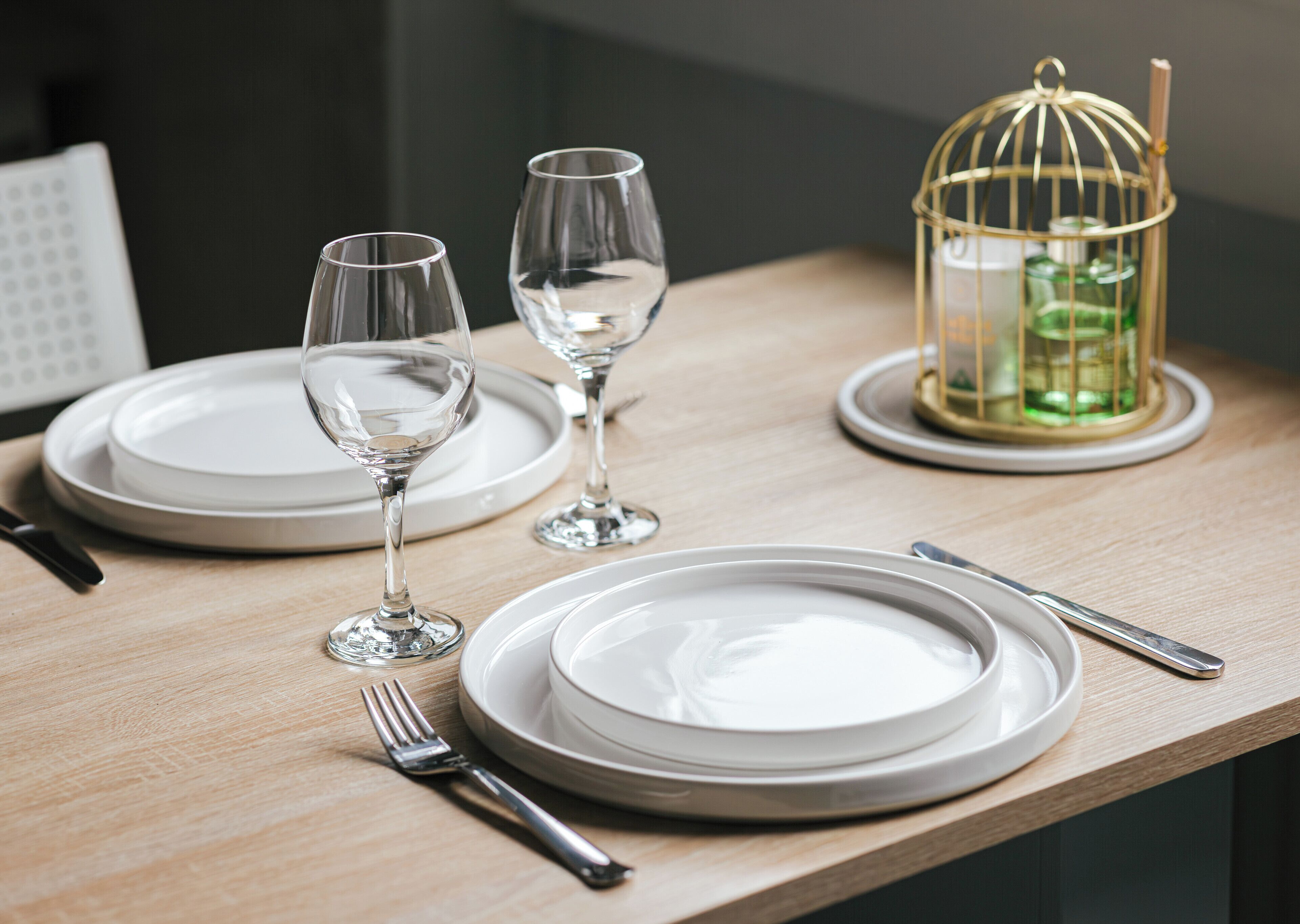 Una mesa de comedor elegantemente dispuesta con platos, vasos, cubiertos y una jaula decorativa.