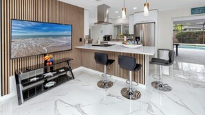 Una cucina moderna con una grande isola, sgabelli da bar e una TV che mostra una spiaggia.