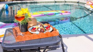 Un tavolino a bordo piscina con un drink, fiori e un piatto di dolci.