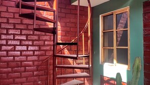 A spiral staircase against a brick wall, a window with a view, and a cactus plant. - Affordable, convenient, and inviting stay in Huaraz. Perfect for groups! (Huaraz)