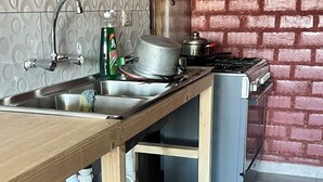 A kitchen with a wooden table, a sink, a stove, and a brick wall. - Affordable, convenient, and inviting stay in Huaraz. Perfect for groups! (Huaraz)