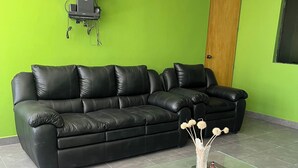 A modern living room with a black leather sofa, a glass coffee table with a green accent, a flat-screen TV mounted on the wall, and a wooden door. - Affordable, convenient, and inviting stay in Huaraz. Perfect for groups! (Huaraz)
