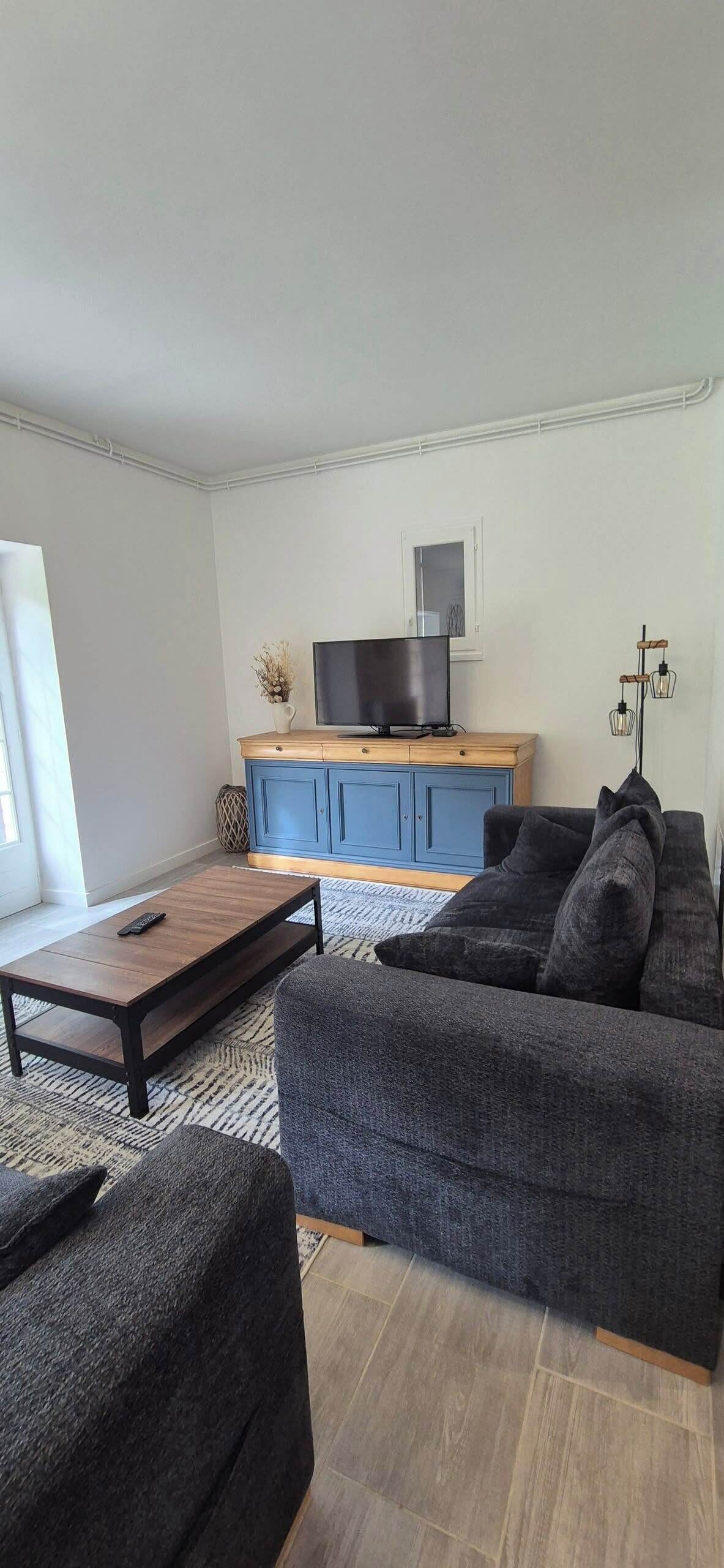 Un salon moderne avec un canapé gris foncé, une table basse en bois et un meuble bleu abritant un téléviseur à écran plat.
