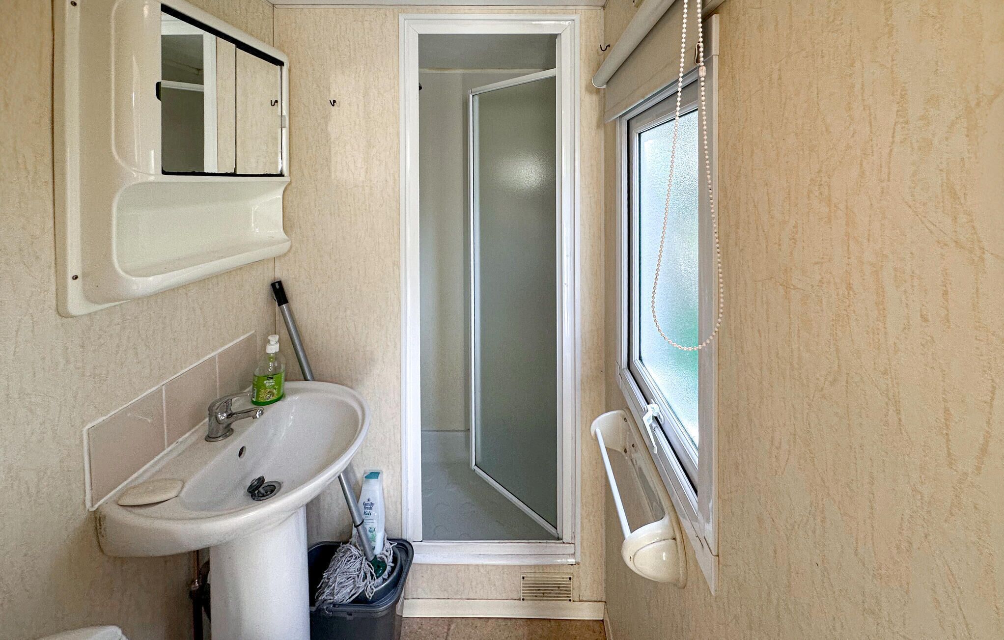 Ein Badezimmer mit Waschbecken, Spiegel, Dusche und Fenster.