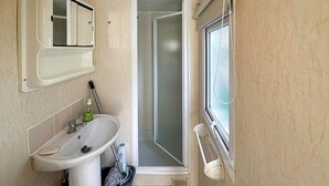 Een badkamer met een wastafel, spiegel, douche en raam.