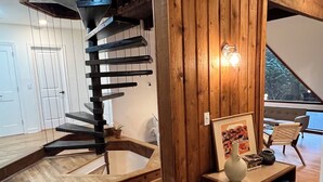 Ein modernes Interieur mit einer Holztreppe, einer Holzwand mit Leuchte und einer Sitzecke mit Vase und Büchern.