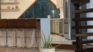 Eine moderne Küche mit einem großen Fenster, weißen Schränken und einer Bar mit Hockern.