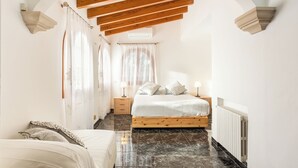 Un dormitorio con techo de madera, una cama con colchón blanco y almohadas estampadas, una mesita de noche con lámpara y un radiador.