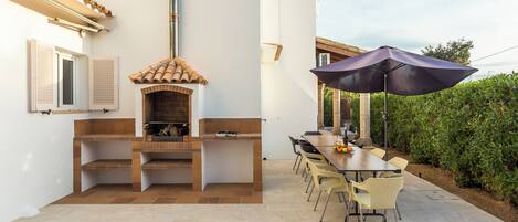 An outdoor patio with a brick barbecue, a dining table with chairs, and a large umbrella.