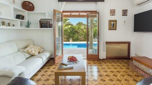 Un salón con un sofá blanco, una mesa de centro con un frutero, y vistas a una piscina al aire libre.